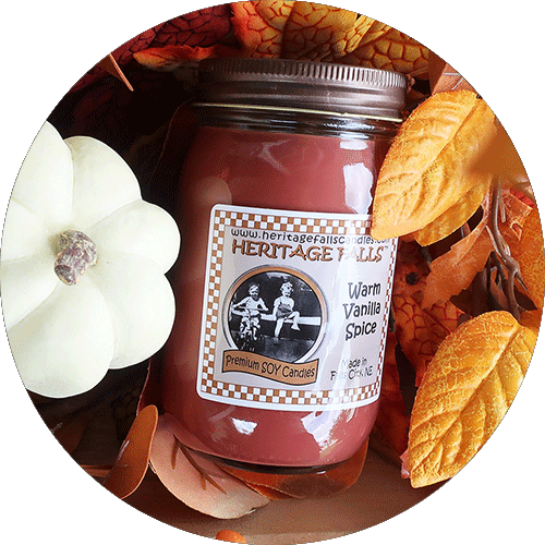 A Warm Vanilla Spice candle next to a white pumpkin and fall leaves.